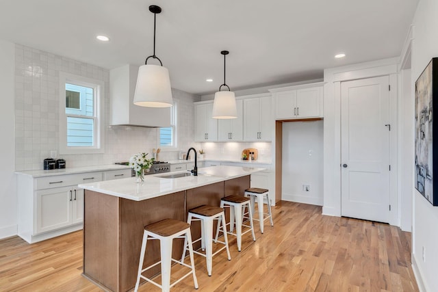 kitchen featuring premium range hood, white cabinetry, a sink, and light wood-style floors