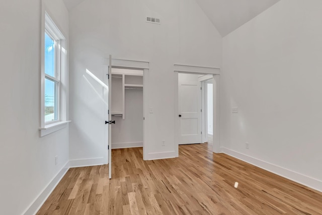 unfurnished bedroom featuring light wood-type flooring, baseboards, visible vents, and high vaulted ceiling