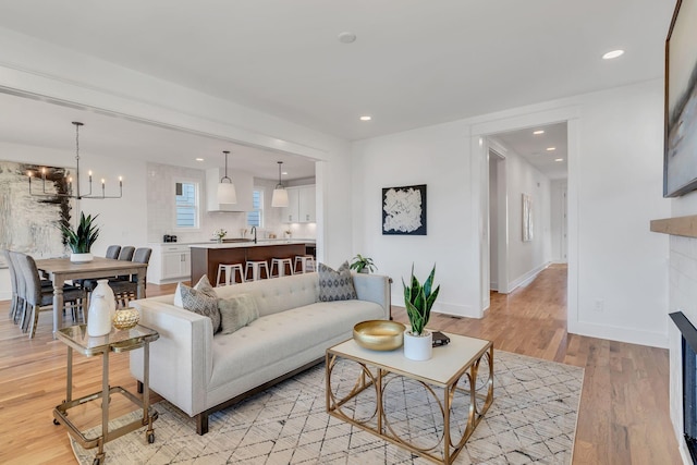 living area with a fireplace, an inviting chandelier, baseboards, and light wood-style flooring