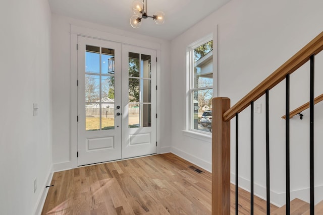 entryway with light wood finished floors, french doors, baseboards, and a chandelier