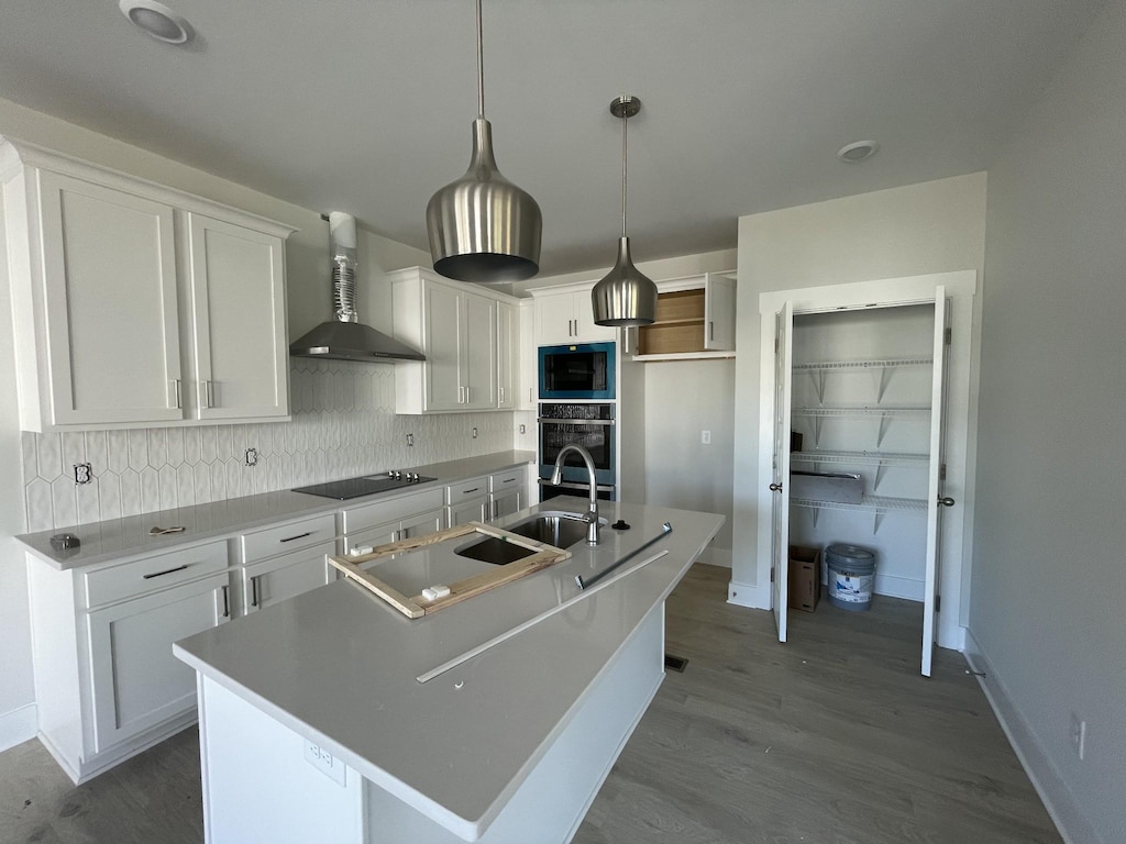 kitchen with white cabinets, backsplash, wall chimney range hood, a sink, and black appliances