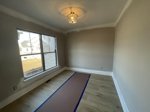 unfurnished room featuring baseboards, wood finished floors, visible vents, and crown molding