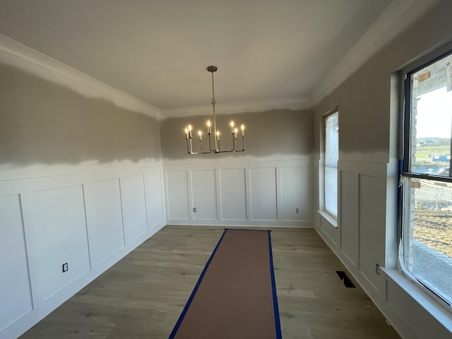 unfurnished dining area featuring a decorative wall, a notable chandelier, wood finished floors, wainscoting, and ornamental molding