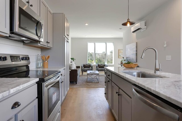 kitchen featuring light wood finished floors, an AC wall unit, a sink, light stone counters, and appliances with stainless steel finishes