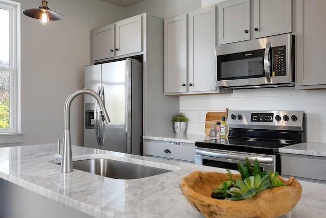 kitchen with appliances with stainless steel finishes, gray cabinets, light stone counters, and a sink