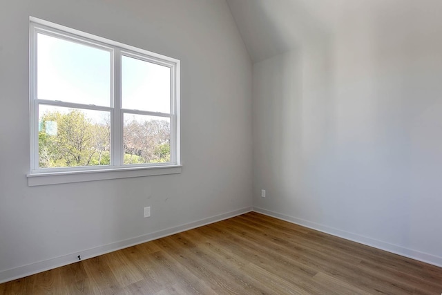 spare room featuring lofted ceiling, baseboards, and light wood-style floors