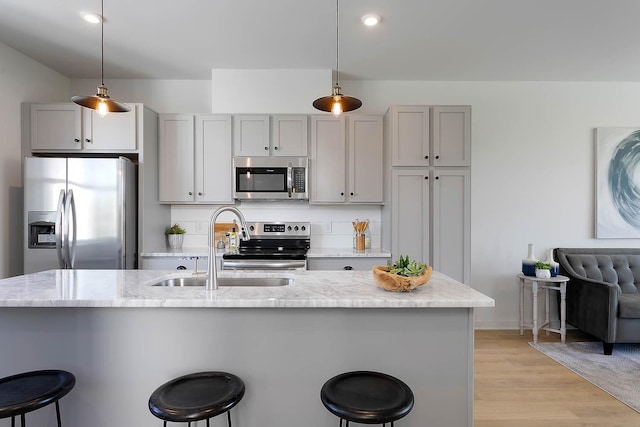 kitchen with stainless steel appliances, a sink, light wood-style floors, gray cabinetry, and a breakfast bar area