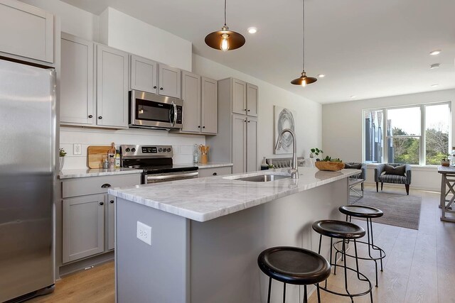 kitchen with stainless steel appliances, open floor plan, a sink, and gray cabinets
