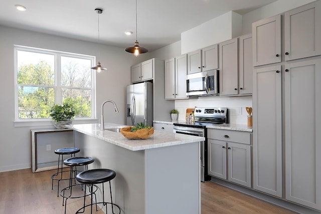 kitchen featuring gray cabinets, a sink, a kitchen bar, light wood-style flooring, and appliances with stainless steel finishes