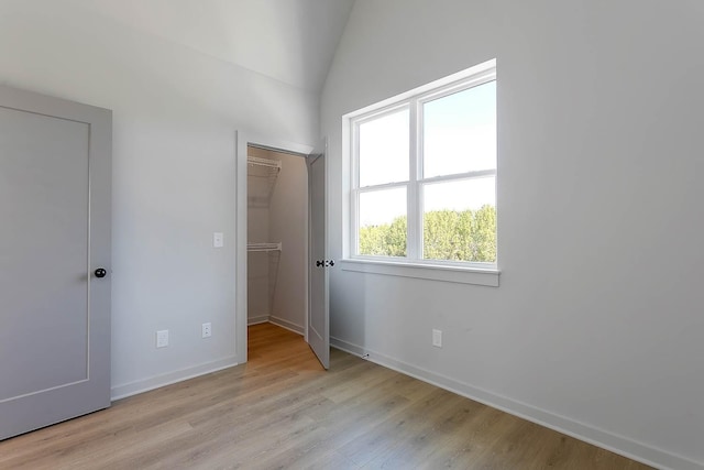 unfurnished bedroom with lofted ceiling, light wood finished floors, a walk in closet, a closet, and baseboards