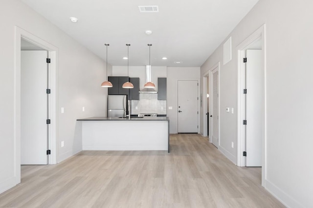 kitchen featuring stainless steel refrigerator, a peninsula, light wood finished floors, wall chimney exhaust hood, and backsplash