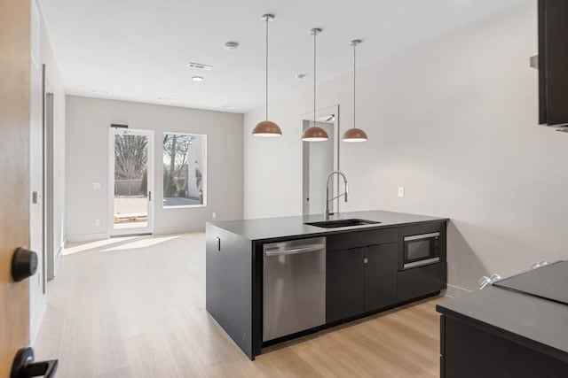 kitchen featuring dishwasher, a sink, light wood-style flooring, dark cabinetry, and dark countertops