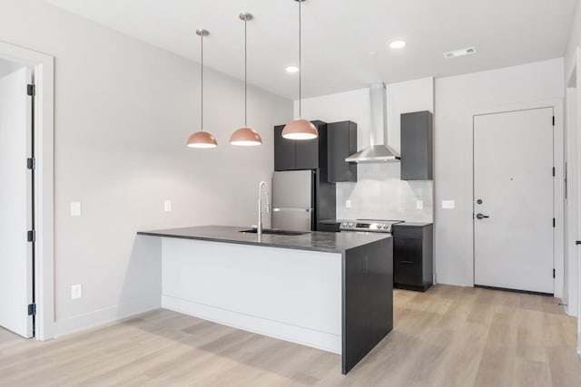 kitchen with wall chimney range hood, light wood-style flooring, a sink, freestanding refrigerator, and recessed lighting