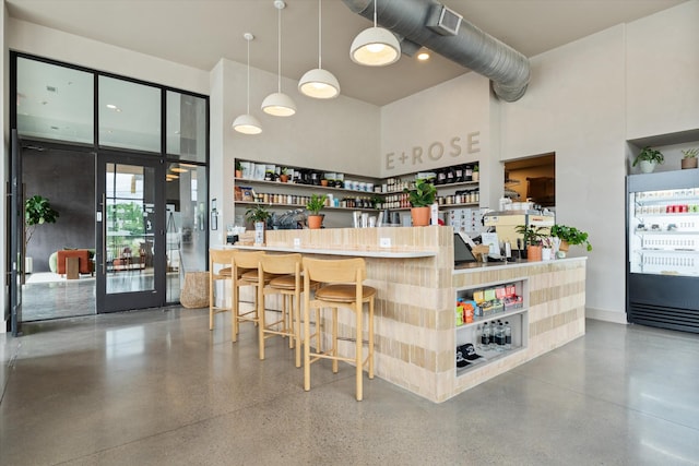 bar area featuring a towering ceiling, speckled floor, and decorative light fixtures