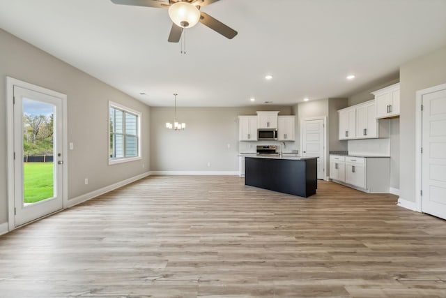 kitchen with ceiling fan with notable chandelier, open floor plan, white cabinetry, baseboards, and appliances with stainless steel finishes
