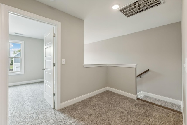 hall featuring carpet floors, visible vents, baseboards, and an upstairs landing