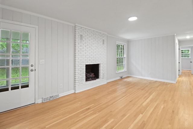 unfurnished living room with light wood-type flooring, baseboards, visible vents, a fireplace, and ornamental molding