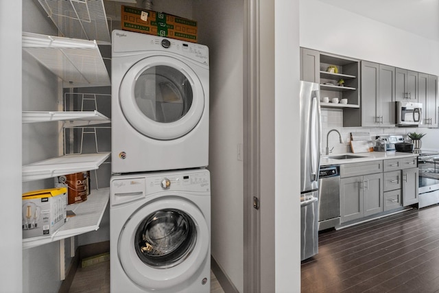 laundry area featuring a sink, laundry area, baseboards, stacked washer / dryer, and dark wood-type flooring