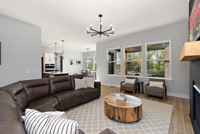 living area with an inviting chandelier, baseboards, and light wood-style flooring