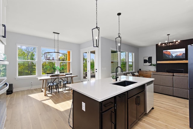 kitchen featuring dark brown cabinetry, light countertops, a sink, light wood-style flooring, and a notable chandelier