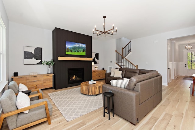 living room with a fireplace, light wood-type flooring, stairs, and a notable chandelier