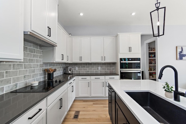 kitchen featuring visible vents, stainless steel double oven, white cabinetry, a sink, and hanging light fixtures