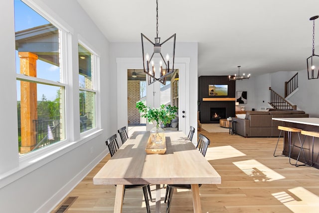 dining space with stairs, a chandelier, plenty of natural light, and light wood finished floors
