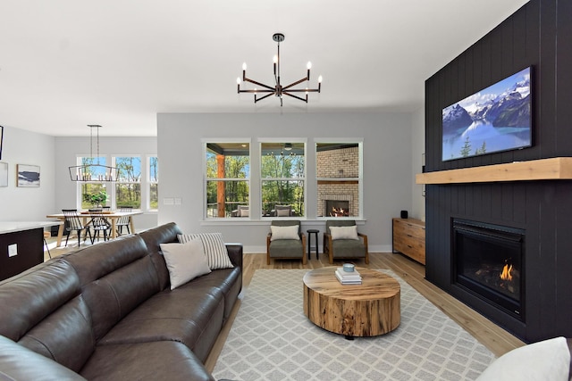 living area with baseboards, light wood-style flooring, a chandelier, and a large fireplace