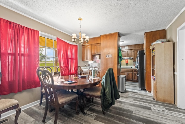 dining space with a textured ceiling, visible vents, ornamental molding, wood finished floors, and a notable chandelier