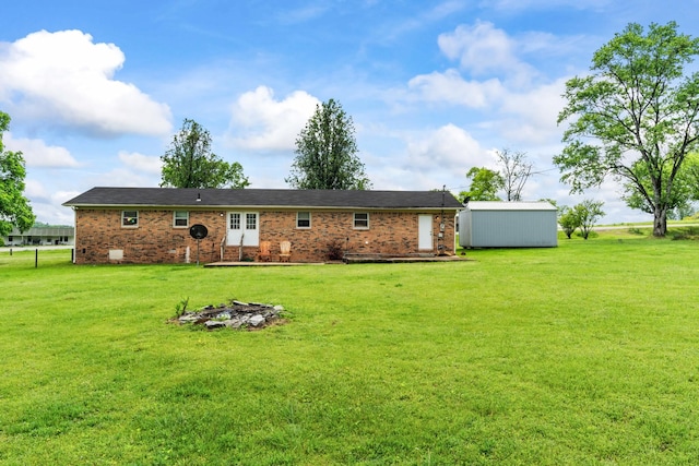 rear view of house with a lawn, a storage unit, brick siding, and an outbuilding