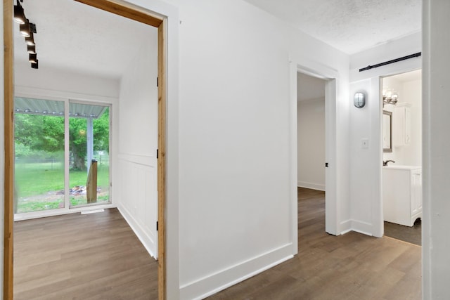 hallway with a barn door, wood finished floors, and a textured ceiling