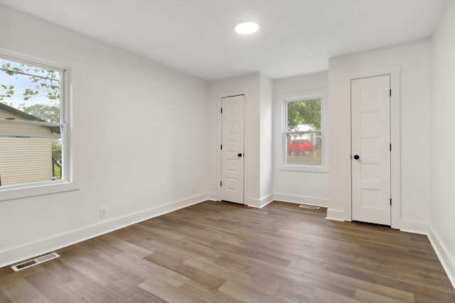 unfurnished room with plenty of natural light, wood finished floors, visible vents, and baseboards