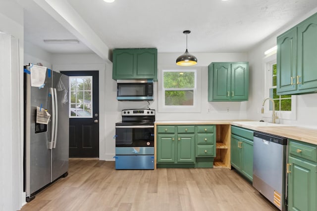 kitchen with stainless steel appliances, a sink, light wood-type flooring, light countertops, and decorative light fixtures