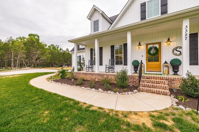 view of exterior entry featuring board and batten siding, a yard, and covered porch