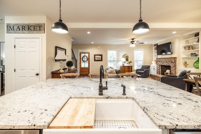 kitchen featuring decorative light fixtures, ceiling fan, a sink, and a fireplace