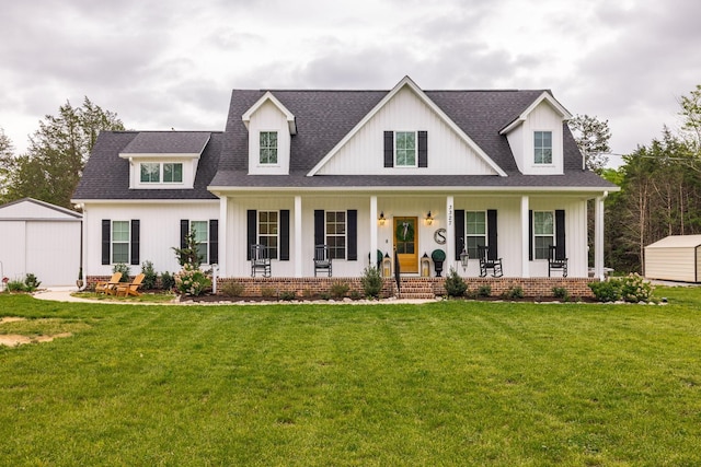 modern farmhouse style home featuring a shingled roof, board and batten siding, an outdoor structure, a porch, and a front yard