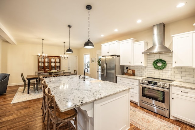kitchen featuring tasteful backsplash, a sink, wall chimney exhaust hood, appliances with stainless steel finishes, and dark wood-style floors