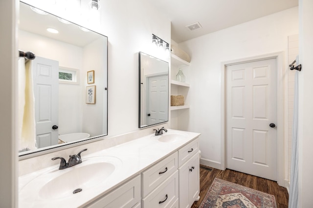 bathroom featuring visible vents, wood finished floors, a sink, and double vanity