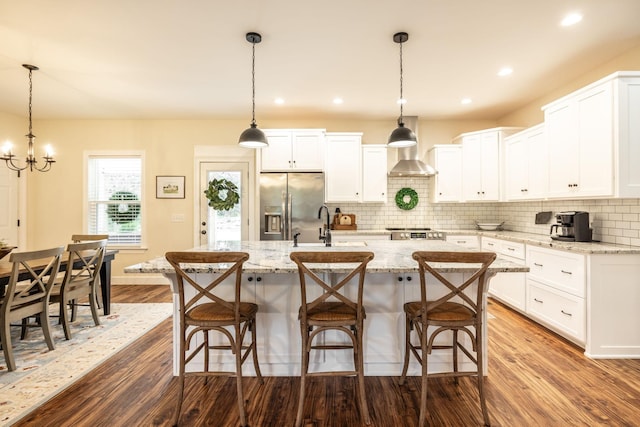kitchen featuring a sink, a center island with sink, decorative backsplash, stainless steel fridge with ice dispenser, and dark wood-type flooring