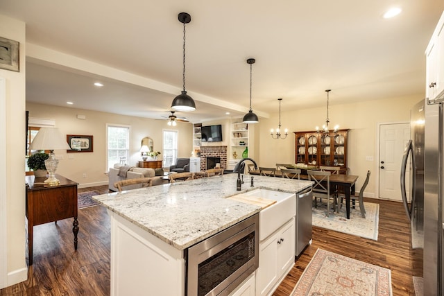 kitchen featuring stainless steel appliances, a sink, dark wood finished floors, white cabinetry, and a brick fireplace