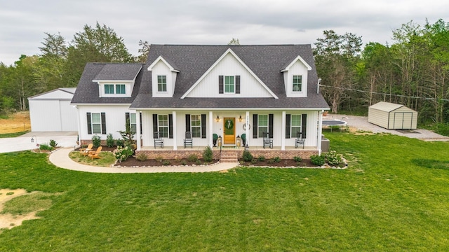 modern inspired farmhouse with a storage shed, a front lawn, an outbuilding, a porch, and roof with shingles
