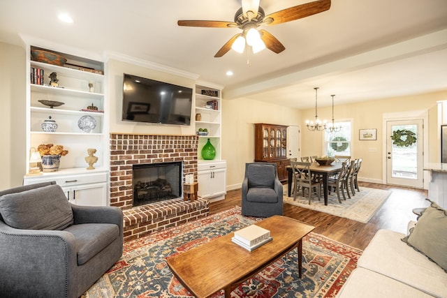living room with wood finished floors, ceiling fan with notable chandelier, baseboards, a brick fireplace, and recessed lighting