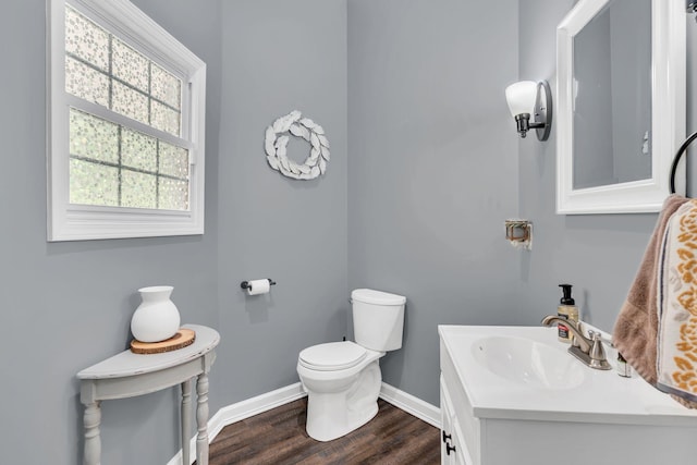 half bath featuring baseboards, vanity, toilet, and wood finished floors