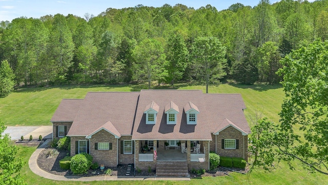 view of front of property with covered porch, brick siding, a wooded view, and a front yard
