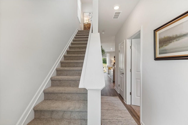 staircase featuring wood finished floors, visible vents, and recessed lighting