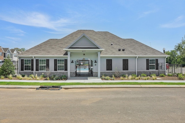 view of front of home featuring a gate, roof with shingles, stone siding, and fence