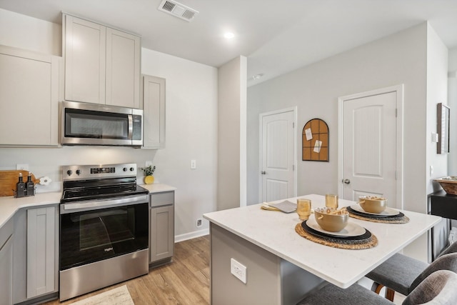 kitchen featuring a kitchen breakfast bar, visible vents, gray cabinets, light wood-type flooring, and appliances with stainless steel finishes