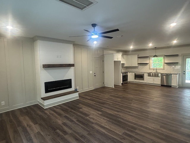 unfurnished living room with visible vents, a fireplace, ceiling fan, a sink, and dark wood finished floors