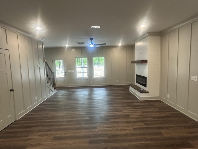unfurnished living room with visible vents, a ceiling fan, a decorative wall, and dark wood-style floors