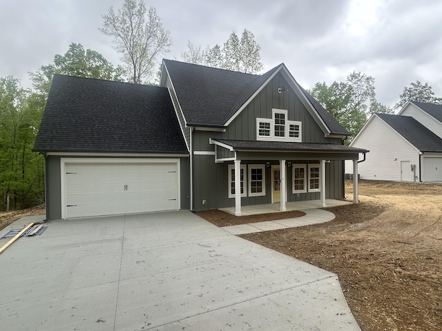 view of front of home with an attached garage, roof with shingles, board and batten siding, concrete driveway, and a porch